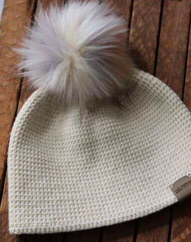 white crochet hat with white pompom laying on a wooden crate
