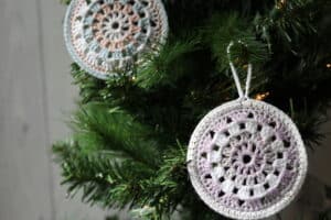 two crochet christmas ornaments hanging on a Christmas tree