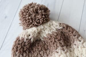 a close up of the top and pompom of the crochet feathers beanie