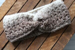 The Feather Stitch Ear Warmer in tan and off white yarn
