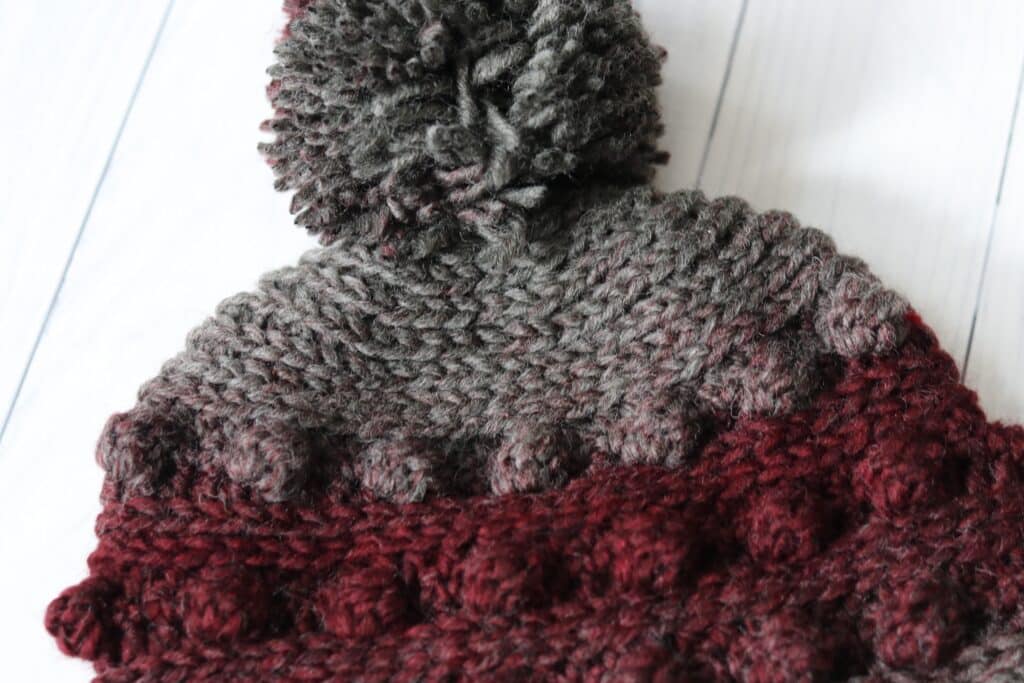 A close up of the crown and pompom on the black cherry crochet beanie