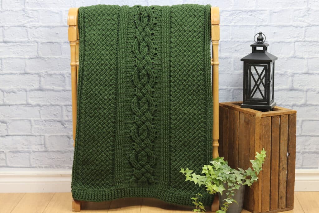 A cable textured crochet blanket worked in green yarn
