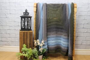 A textured blue and green crochet blanket on a quilt rack
