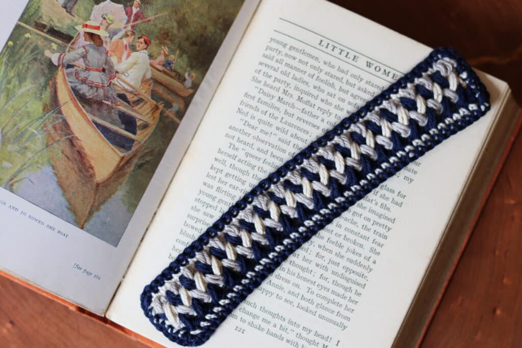 A blue, white and grey crochet bookmark that looks like it woven