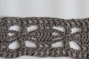 A lacy crochet stitch pattern featuring chains and cluster stitches that resembles marching ants