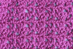 A swatch of the V and Three crochet stitch pattern worked in a vibrant pink yarn