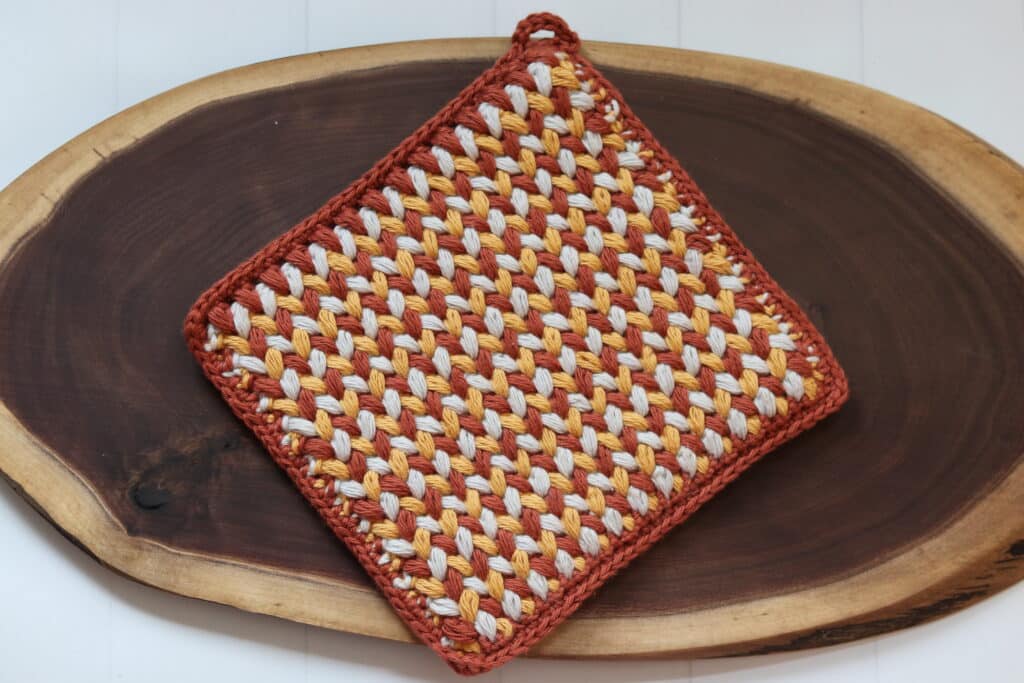 A brown, yellow and grey crochet hot pad worked in the spiked puff stitch