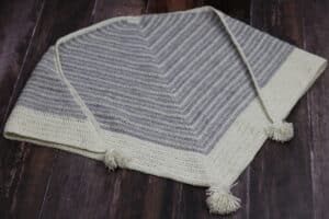 A triangular crochet shawl with grey and white stripes