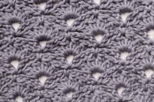 A lacy shell crochet stitch comprised of double crochet cluster stitches and worked in a grey yarn