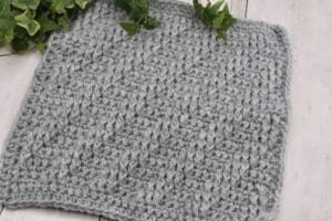 A crochet afghan square featuring diagonal cables and worked in a grey yarn