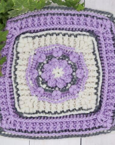 A textured crochet afghan square in purple, white and grey yarn