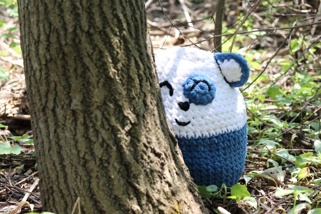 Brady the crochet bear peeking out from behind a tree