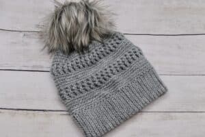 A textured crochet hat worked in a grey coloured yarn with a tan coloured pompom