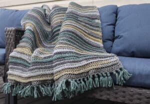 Crochet blanket featuring gold, greys and green draped over a couch