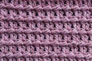 A swatch of the V and Cluster crochet stitch worked in pink yarn