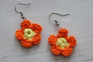 A pair of crocheted flower earrings worked in orange yarn with a yellow centre