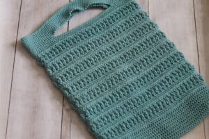A textured crochet market bag laid flat and worked in green yarn