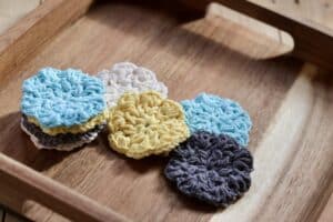A set of crochet face scrubbies displayed on a wooden tray