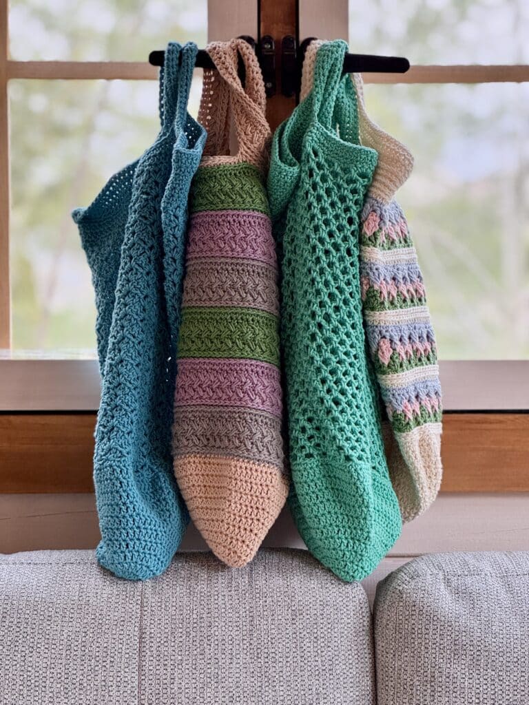 A collection of four crochet market bags hanging in a window