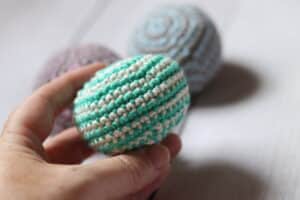 a hand holding a green and white stripped crochet footbag
