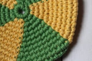 A close up image of a yellow and green crochet pocket flying disc