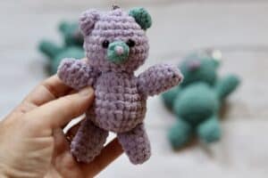A woman's hand holding a small, crochet teddy bear key chain
