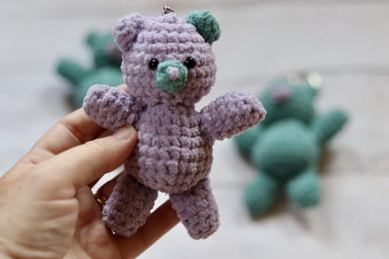 A woman's hand holding a small, crochet teddy bear key chain